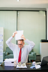 Senior businessman rips paperwork in rage at office desk. Workplace stress, anger, chaos, and...