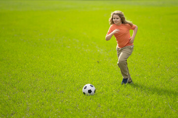 Obraz premium Kid playing football in the park. Child kicking a football ball on field. Happy boy running with a football ball. Children playing soccer outdoors. Kid play football on the grass. Summer soccer game.