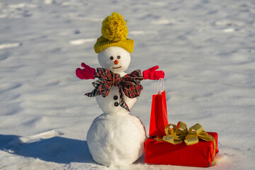 Snowman with Christmas present gift box outdoor. Funny snowman with a carrot nose and scarf and...