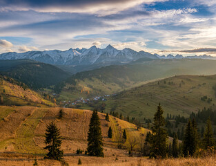 Tatras village in the autumn mountain valley. Autumn mountain village, with a beautiful autumn sun, snowy mountain peaks in the background. Mountain village in autumn landscape. Polskie gory