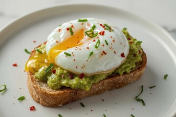 Avocado toast topped with a poached egg, sprinkled with chives and red pepper flakes on a white plate.
