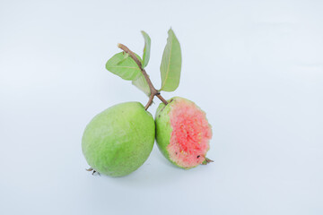 Fresh ripe pink guava (Psidium guajava) fruit, one whole and one half-eaten, attached to a twig...