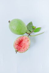 Fresh ripe pink guava (Psidium guajava) fruit, one whole and one half-eaten, attached to a twig...