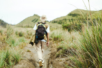Blurred back view of a solo hiker with backpack walking Bromo grass hills
