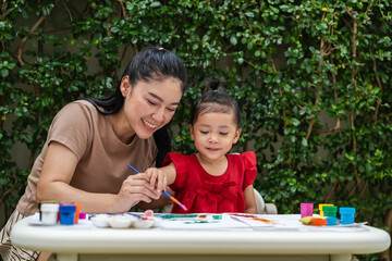 happy mother and toddler girl painting watercolor in paper at backyard.