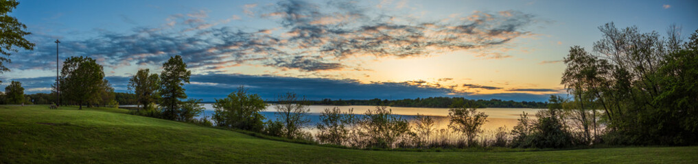 Sunset over calm river with trees and green grass