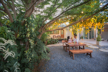 Obraz premium A heartwarming moment of a father and daughter sitting at a wooden table under a blooming golden shower tree.
