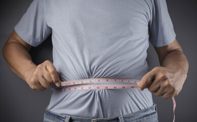 Overweight or obese man with abdominal fat using a tape measure to check his waist size, Health and...