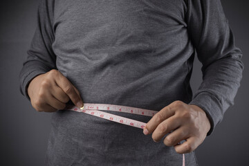 Overweight or obese man with abdominal fat using a tape measure to check his waist size, Health and...
