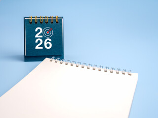 Happy new year 2026. 2026 numbers with target dart icon on blue desk calendar cover, standing near white blank notepad, empty space note page for memo. Business goal, resolutions and success concept.