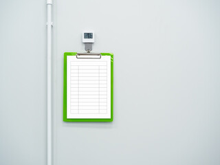 Clipboard checklist table white paper and LED digital instrument wall mounted warehouse temperature humidity sensor detection industry monitor meter, on white clean wall background with copy space.