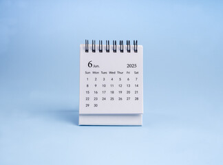 A June 2025 desk calendar for organizer to plan and reminder standing, isolated on blue horizontal background, minimalist. White small table calendar with the page of the sixth month, minimal style.
