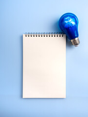 Creative idea and inspiration with AI assistant service technology concept. AI chatbot icon on electric lightbulb and mockup empty white blank space of vertical spiral notebook page, blue background.