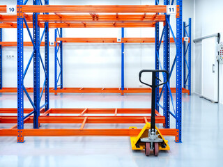 Yellow hand pallet truck or hydraulic pallet jack, parked near rack, steel shelves, ready to loading goods, in warehouse. Manual Hand Lift. Pallet Jack Loader. Industry tools and equipment concept.