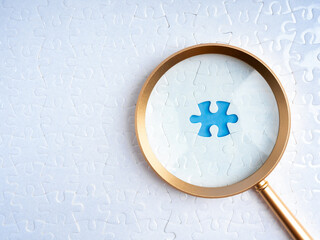 HR, human resources, recruitment and hiring, problem solving solution, business strategy concept. Blue space for last missing piece, focus in magnifying glass lens, on white jigsaw puzzle background.