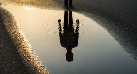 Person reflection in water puddle on asphalt during hot day. Heat waves and urban temperature effects for summer weather awareness