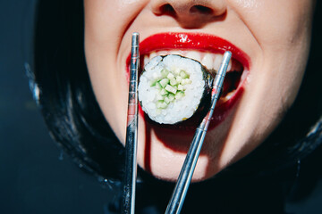 Young woman enjoying sushi with vibrant red lipstick and chopsticks, showcasing a playful culinary...
