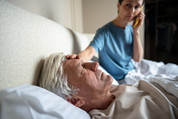 Exhausted feverish man lying with high temperature, woman calling emergency help touching burning...