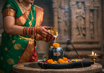 South Asian Woman Performing Shiva Lingam Ritual with Holy Water in Traditional Temple Setting