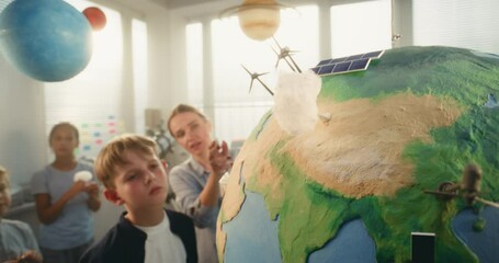 Environmental Science Lesson: Female Teacher Educating Renewable Energy to Team of Smart Kids in Multiethnic Classroom. Primary School Boy Attaching Miniature Cloud to Earth Model. STEM Education. - Powered by Adobe