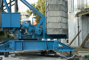 Construction crane base with blue mechanical components and stacked concrete counterweights on active construction site highlighting engineering detail and safety context.