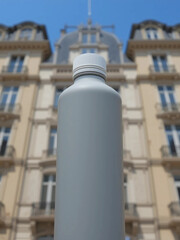 A gray, unlabeled bottle stands in the foreground, with a blurred-out elegant building in the background. Perfect for product mockups.