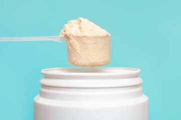 Protein powder in scoop and plastic jar on blue background.