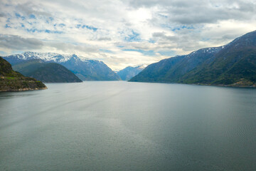 Hardanger Bridge spans serene waters with large white cruise ship. Surrounding landscape features...