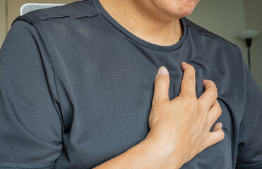 An Asian man clutches his chest with visible discomfort, indicating possible cardiac or respiratory...