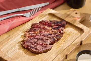 Ribeye steak sliced, premium marbled beef on rustic bright wooden board, overhead composition