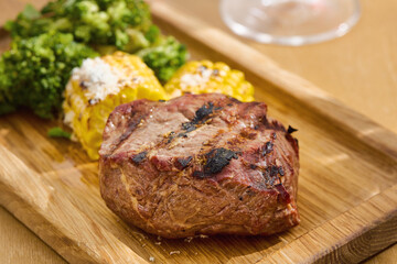 Filet mignon steak with grilled corn and broccoli, bright lighting, rustic overhead composition
