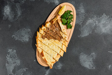 Cheese and meat pide mix, bright lighting, overhead composition on dark textured surface