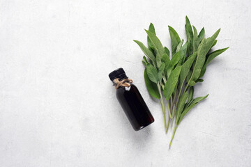 Bottle of essential sage oil and sage leaves, on white background. top view,copy space