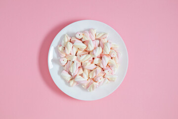 Background with multicolored marshmallows spirals in a white round plate in the center of the background. Top view. Flat lay.