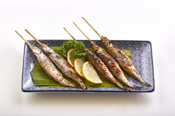 Grilled shishamo fish skewers served on decorative plate with lemon slices and parsley garnish, creating delicious and appetizing presentation