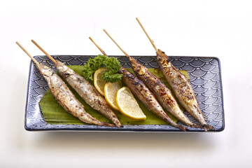 Grilled shishamo fish skewers served on decorative plate with lemon slices, parsley garnish, and banana leaf base, showcasing traditional Japanese dish