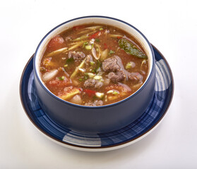 Flavorful bowl of spicy beef shank soup with tender beef pieces, fresh tomatoes, herbs, and spices served in blue ceramic bowl on matching plate