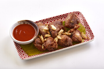 Crispy fried pork served on decorative plate with banana leaf, garnished with fried garlic, and accompanied by bowl of tangy red dipping sauce