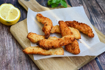 
 Crispy home made  deep fried   chicken strips . Breaded  with cornflakes chicken  breast fillets  with chilly peppers and fresh   basil on wooden rustic background