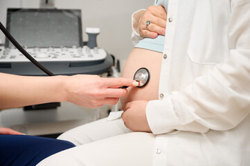 Cropped view of doctor listening to a pregnant woman's belly with a stethoscope during medical...