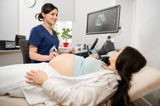 Female doctor performing prenatal ultrasound scan on pregnant woman at clinic. Modern obstetric care and pregnancy checkup with sonography.