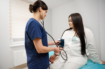 Female doctor measuring blood pressure of pregnant woman in medical clinic. Obstetrician measuring blood pressure of the pregnant woman in the hospital. Pregnancy induced hypertension concept.