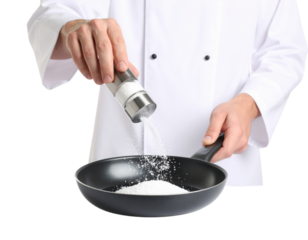 A chef sprinkles salt from a shaker into a frying pan while holding the pan's handle with the other hand.