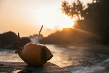 Coconut with straw resting on wooden surface, overlooking tranquil ocean waves during a vibrant...