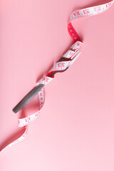 A fork entwined with a pink measuring tape rests on a pale pink background.Dietary Control Concept
