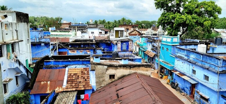 The unique charm of Indian housing, showcasing a mix of vibrant blue facades, traditional tile roofs, and corrugated metal structures in a bustling village setting under cloudy sky