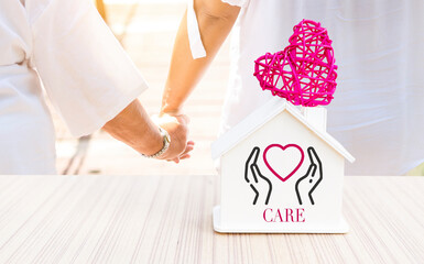 Elderly care home service concept, miniature house with pink heart over blurred girl holding hand...