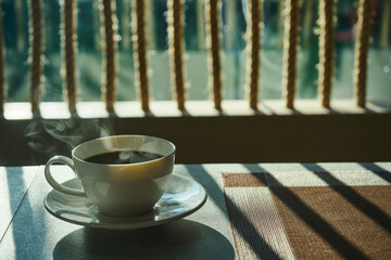 a morning hot coffee in white cup in sunshine scene with shade and white smoke from hot water