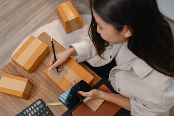 an entrepreneur is packing parcel for order from customer, she own a small business, sme, a lot of package in the room, e-business is running by a this entrepreneur, online shopping