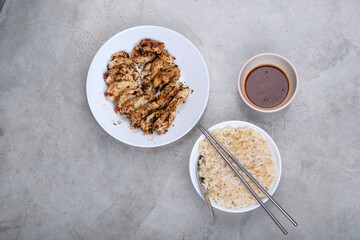 Chicken steak served with rice and dipping sauce on a raw concrete table